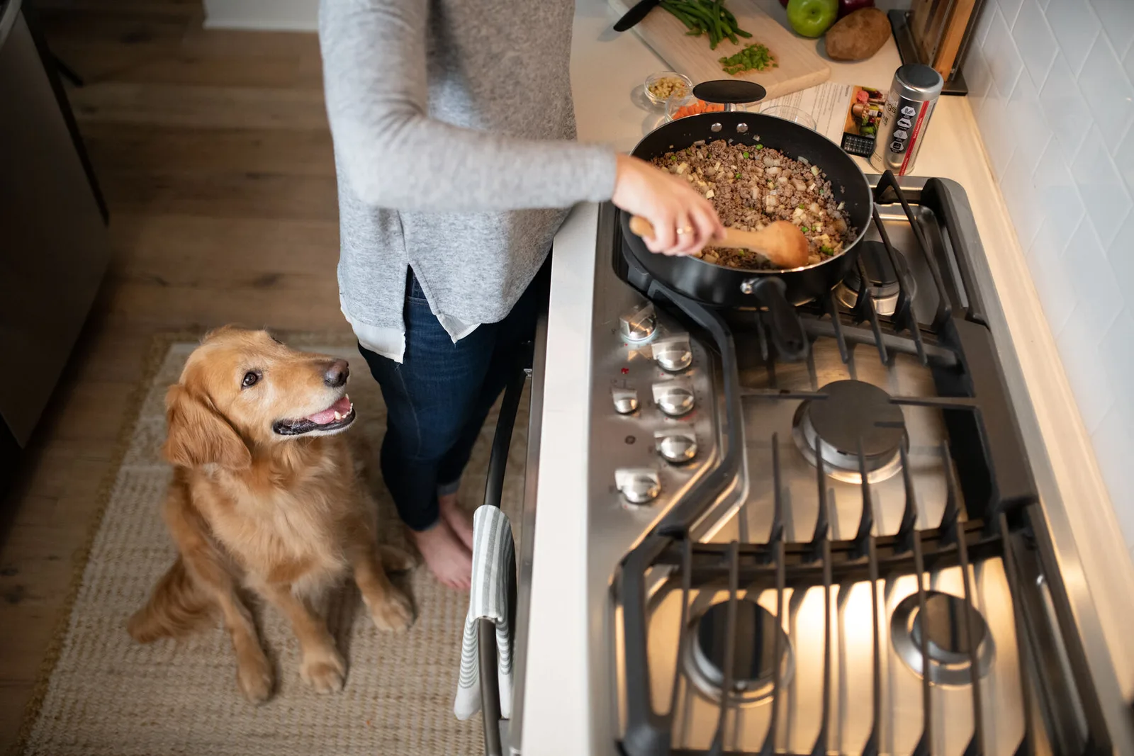 Pet parent cooks a batch of homemade dog food on the stovetop while a golden retriever watches