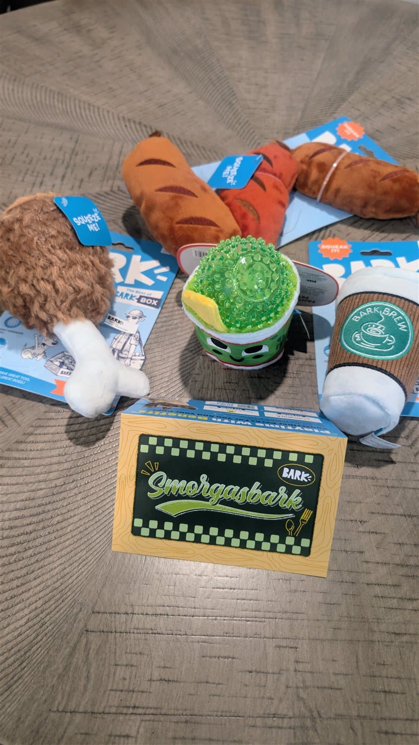 Flat lay of a BarkBox Smorgasbark box with food-themed plush toys and treats