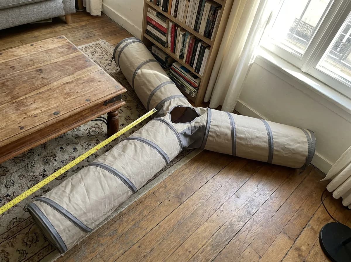 Three-way fabric cat tunnel spread across a living room floor beside a coffee table with a tape measure laid along one arm