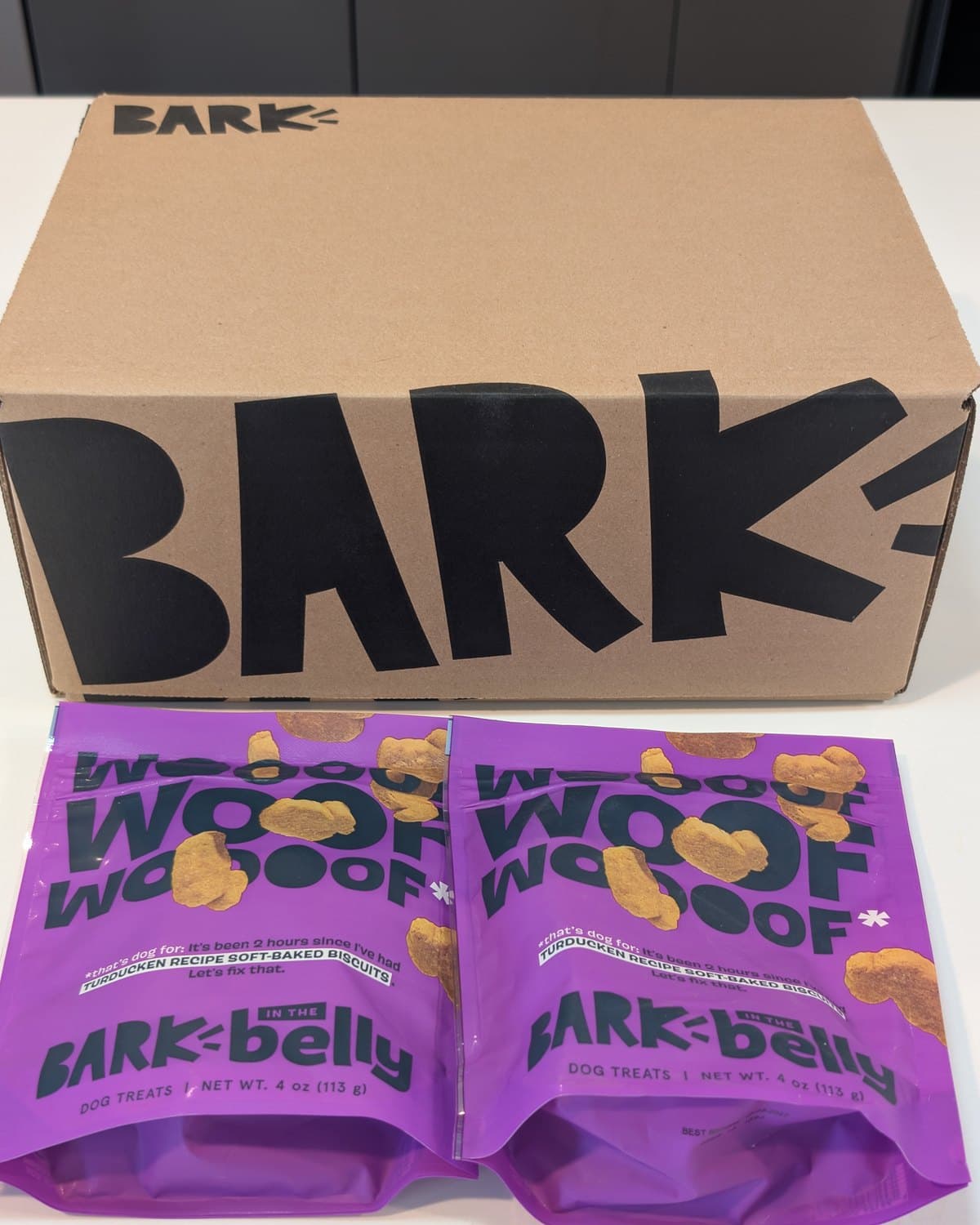 BarkBox shipping carton as delivered with two purple BARK treat pouches on top
