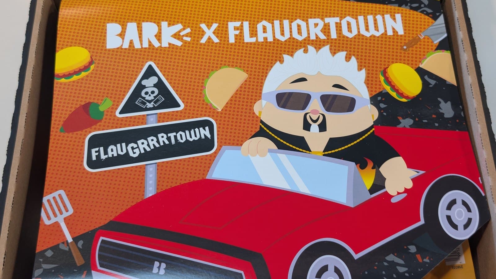 BARK x Flavortown theme card with cartoon Guy Fieri in a red car inside the opened BarkBox