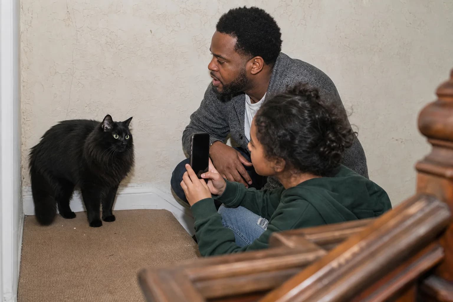 Father and child observing a long-haired black cat's response to a spoken name