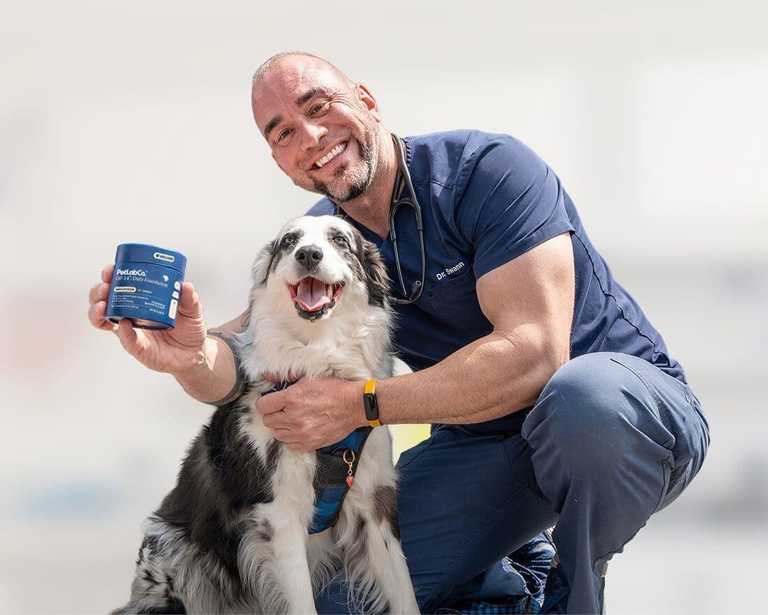 A man in navy scrubs holds a DF-14 tub beside a black-and-white dog.