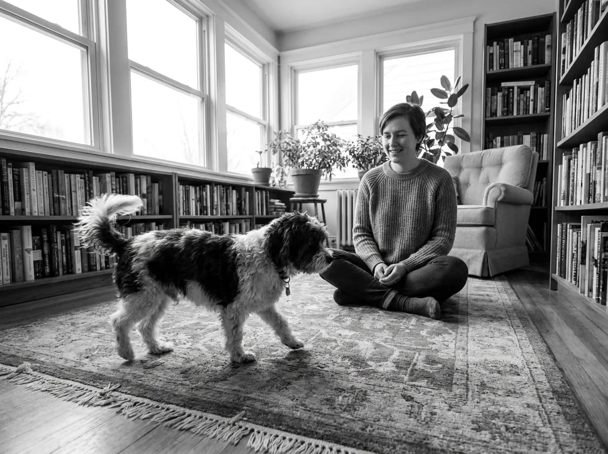 Black-and-white photograph of a small dog approaching a seated person in a reading room