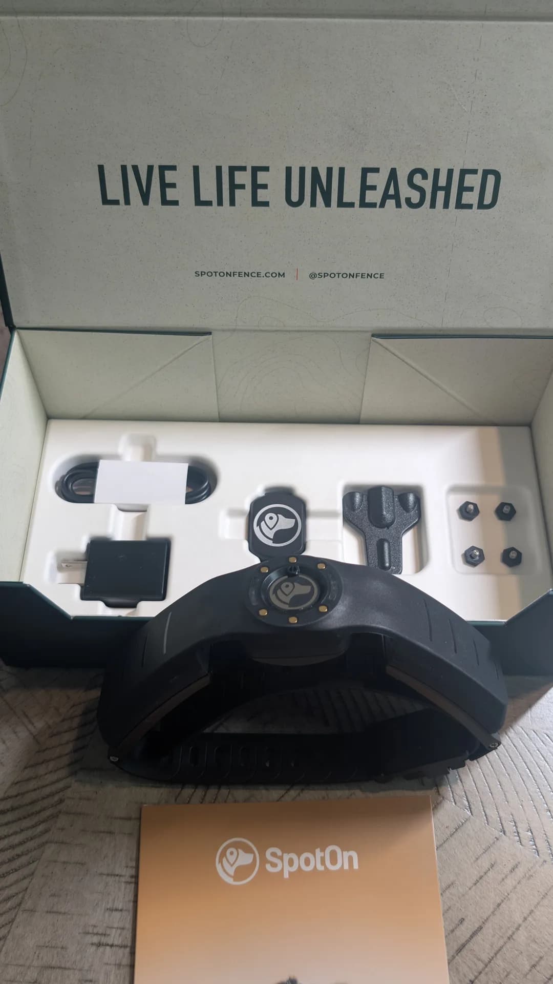 The SpotOn GPS dog collar folded in front of its open box and accessory tray during unboxing.