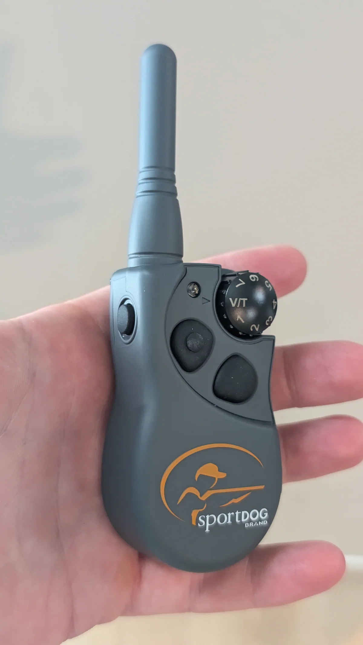 SportDOG 425X transmitter in hand with intensity dial and three buttons visible
