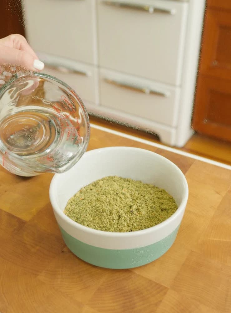 A measuring jug of water held over a bowl of Honest Kitchen Wholemade dehydrated food
