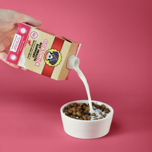 Pouring Brutus Broth goat milk over dog kibble as a nutritious meal topper.