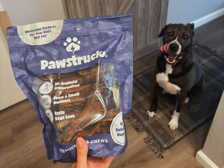 A bag of Pawstruck dog treats in front of a brown and white dog.